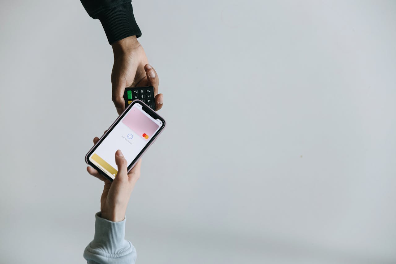 Hands using smartphone and terminal for cashless payment, showcasing modern transaction methods.
